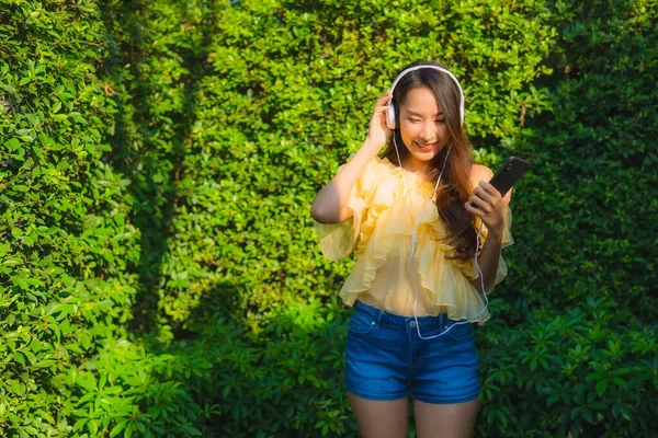 年轻的亚洲女人使用智能手机和耳机聆听户外花园自然景观的音乐 — 图库照片