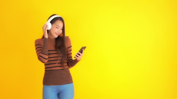 Záběry Krásné Asijské Ženy Poslech Hudby Smartphone Sluchátka Izolované Žluté — Stock video
