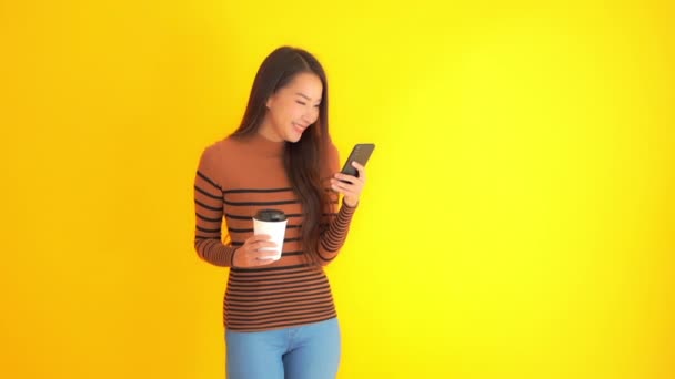 Záběry Krásné Asijské Ženy Smartphone Papírový Šálek Kávy Izolované Žluté — Stock video