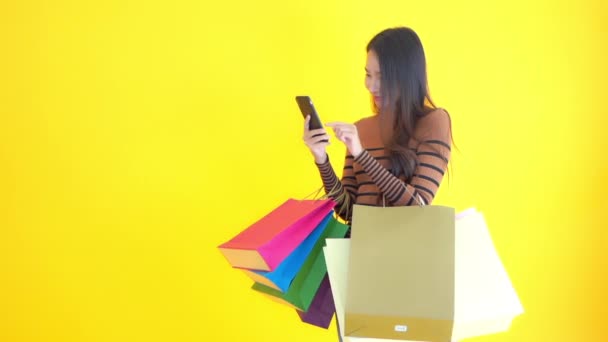 Beeldmateriaal Van Mooie Aziatische Vrouw Met Smartphone Kleurrijke Boodschappentassen Geïsoleerd — Stockvideo