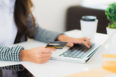 Güzel bir Asyalı kadının portresi online alışveriş malzemesi olarak dizüstü bilgisayarla kredi kartı kullanıyor.