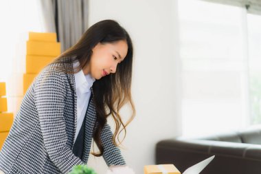 Güzel Asyalı iş kadını portresi evden bilgisayarlı cep telefonuyla karton kutuyla çevrimiçi alışveriş için hazır bekliyor.