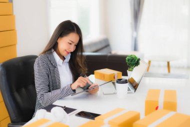 Güzel Asyalı iş kadını portresi evden bilgisayarlı cep telefonuyla karton kutuyla çevrimiçi alışveriş için hazır bekliyor.