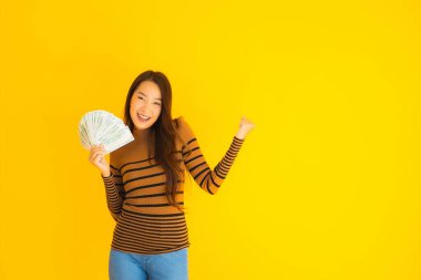 Güzel, genç Asyalı bir kadının portresi mutlu bir gülümseme ve sarı izole edilmiş arka planda bir sürü parası var.