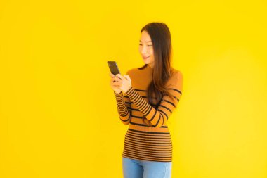 Güzel genç Asyalı kadın, sarı izole edilmiş arka planda birçok eylem içeren akıllı cep telefonu ya da cep telefonu kullanır.