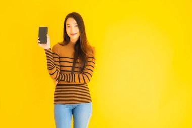 Güzel genç Asyalı kadın, sarı izole edilmiş arka planda birçok eylem içeren akıllı cep telefonu ya da cep telefonu kullanır.