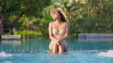 Güzel Asyalı bir kadının, tatil için otel tatil beldesinde yüzme havuzunda dinlendiği görüntüler.