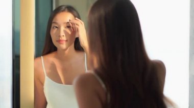 Güzel Asyalı bir kadının banyodaki aynaya bakarken makyaj yaptığı görüntüler.