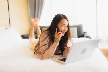 Yatak odasının iç kısmında dizüstü bilgisayarı ve cep telefonu olan güzel Asyalı kadın portresi.