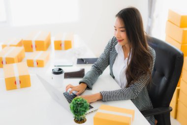 Güzel Asyalı iş kadını portresi evden bilgisayarlı cep telefonuyla karton kutuyla çevrimiçi alışveriş için hazır bekliyor.