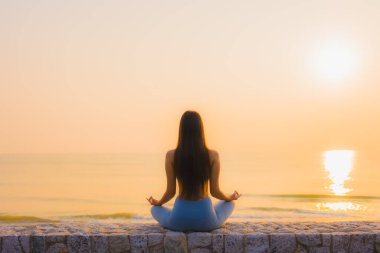 Genç Asyalı kadının portresi sağlık için gün doğumunda deniz kıyısı okyanusunda meditasyon yapıyor.