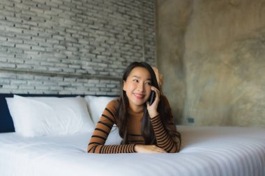 Genç Asyalı kadın yatak odasının iç kısmında cep telefonu kullanıyor.