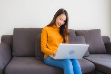 Genç Asyalı bir kadının oturma odasında çalışmak için dizüstü bilgisayar defteri kullanmasının portresi.