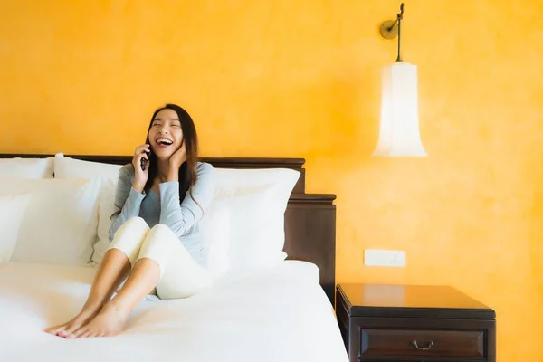 Portrait beautiful young asian woman using mobile cell phone on bed with coffee cup in bedroom interior