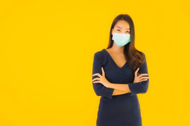 Koronavirüsten korunmak için maske takmış güzel Asyalı bir kadın portresi ve sarı izole edilmiş arka planda 19 numara.