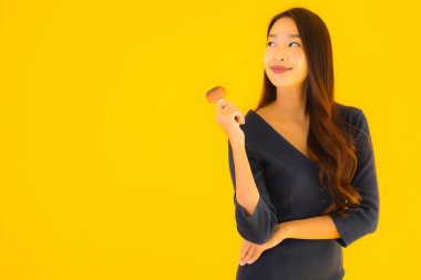 Sarı izole arkaplanda makyaj fırçası olan güzel bir Asyalı kadın portresi.