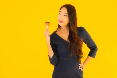 Sarı izole arkaplanda makyaj fırçası olan güzel bir Asyalı kadın portresi.
