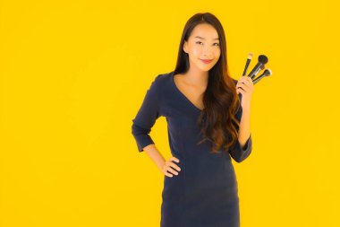 Sarı izole arkaplanda makyaj fırçası olan güzel bir Asyalı kadın portresi.