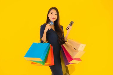 Portre güzel genç Asyalı kadın alışveriş çantası kredi kartı ve akıllı cep telefonu sarısı izole bir arka plan.