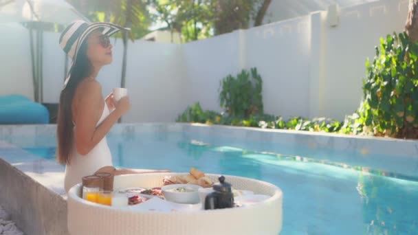 在酒店度假胜地的游泳池里 年轻的亚洲女人开心地笑着享受漂浮的早餐盘的镜头 — 图库视频影像