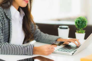 Güzel bir Asyalı kadının portresi online alışveriş malzemesi olarak dizüstü bilgisayarla kredi kartı kullanıyor.