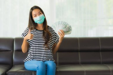 Maskeli güzel Asyalı kadının portresi evde para ya da para gösteriyor.