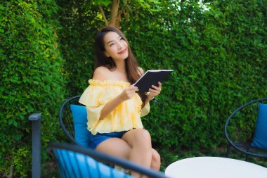 Genç Asyalı kadın bahçe manzarası hakkında kitap okuyor.