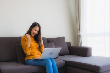 Genç Asyalı bir kadının oturma odasında çalışmak için dizüstü bilgisayar defteri kullanmasının portresi.