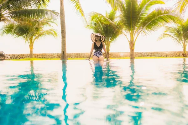 Güzel bir Asyalı kadın portresi, gün batımında palmiye ağacıyla birlikte havuz kenarında dinleniyor ya da tatil için gün doğumunda dinleniyor.