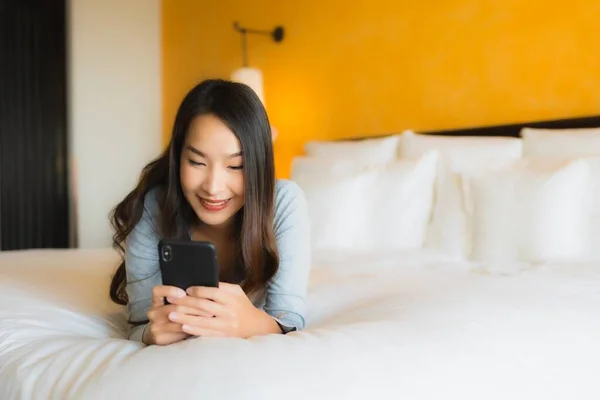 Portrait beautiful young asian woman using mobile cell phone on bed with coffee cup in bedroom interior