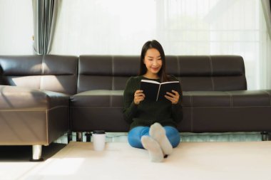 Güzel bir Asyalı kadın portresi. Oturma odasında kahve fincanı ve kanepeyle kitap okuyor.
