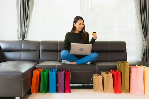 漂亮的年轻亚洲女人在家里用手提电脑和带有购物袋的信用卡进行网上购物 — 图库照片