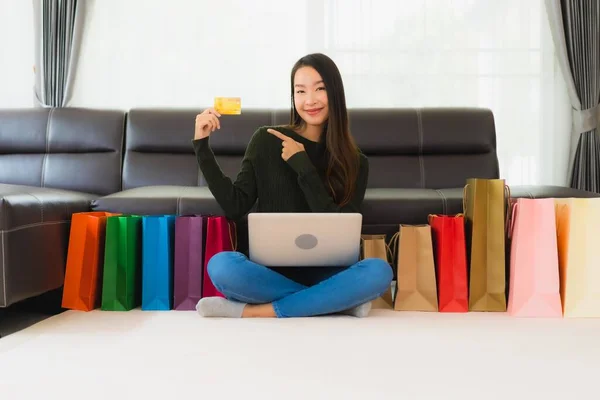 漂亮的年轻亚洲女人在家里用手提电脑和带有购物袋的信用卡进行网上购物 — 图库照片