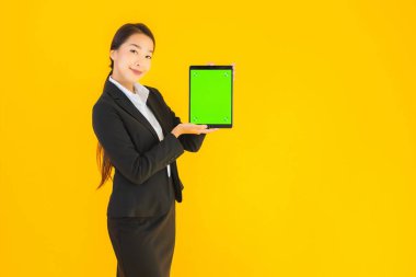 Güzel, genç Asyalı bir kadının portresi mutlu bir gülümseme ve sarı izole edilmiş arka planda akıllı tabletler.