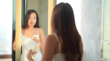 Güzel Asyalı bir kadının banyodaki aynaya bakarken makyaj yaptığı görüntüler.