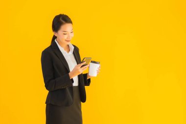 Portre güzel genç Asyalı kadın akıllı cep telefonu ve kahve fincanı ile izole edilmiş sarı arka planda