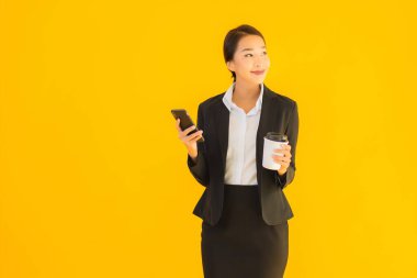Portre güzel genç Asyalı kadın akıllı cep telefonu ve kahve fincanı ile izole edilmiş sarı arka planda