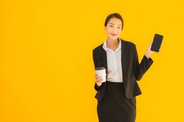Portre güzel genç Asyalı kadın akıllı cep telefonu ve kahve fincanı ile izole edilmiş sarı arka planda