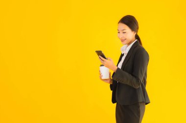 Portre güzel genç Asyalı kadın akıllı cep telefonu ve kahve fincanı ile izole edilmiş sarı arka planda