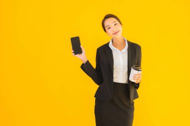 Portre güzel genç Asyalı kadın akıllı cep telefonu ve kahve fincanı ile izole edilmiş sarı arka planda
