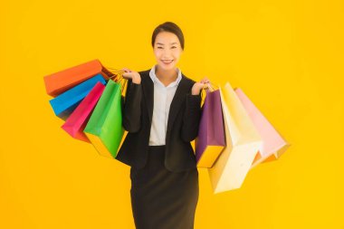 Sarı izole edilmiş arka planda alışveriş merkezinden alışveriş çantasıyla güzel bir genç Asyalı kadın portresi.