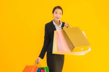 Sarı izole edilmiş arka planda alışveriş merkezinden alışveriş çantasıyla güzel bir genç Asyalı kadın portresi.