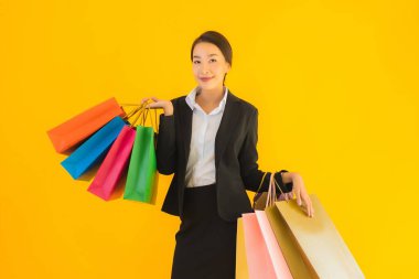 Sarı izole edilmiş arka planda alışveriş merkezinden alışveriş çantasıyla güzel bir genç Asyalı kadın portresi.