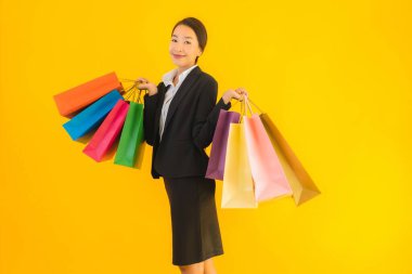 Sarı izole edilmiş arka planda alışveriş merkezinden alışveriş çantasıyla güzel bir genç Asyalı kadın portresi.