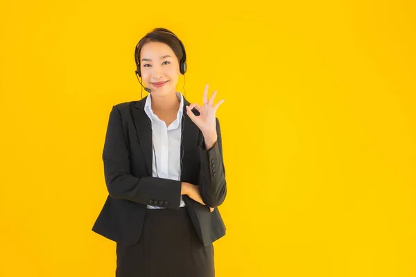 黄色の隔離された背景にコールセンターやテレマーケティングのためのヘッドフォンやヘッドセットを持つ肖像画の美しい若いビジネスアジアの女性 — ストック写真