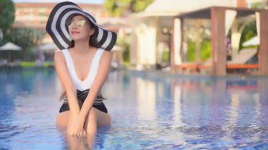 Güzel Asyalı bir kadının, tatil için otel tatil beldesinde yüzme havuzunda dinlendiği görüntüler.