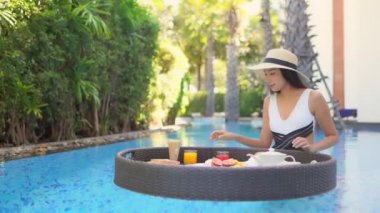 Güzel Asyalı bir kadının, tatil için otel tatil beldesinde yüzme havuzunda dinlendiği görüntüler.