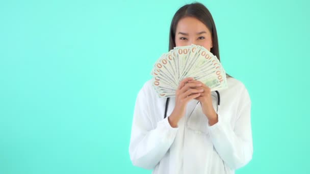 トルコ石で隔離された現金を持っている美しいアジア系女性医師の映像 — ストック動画