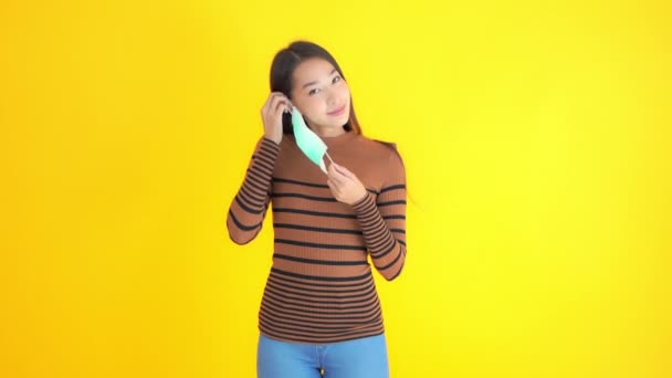 Metraje Hermosa Asiático Mujer Poniendo Médico Protección Máscara Aislado Amarillo — Vídeos de Stock