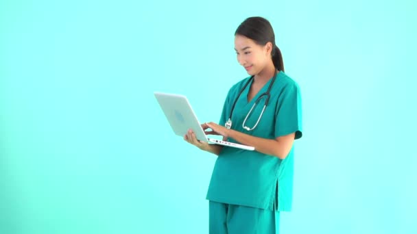 ポートレート美しいです若いアジアの医師女性使用してノートパソコン上の青隔離された背景 — ストック動画